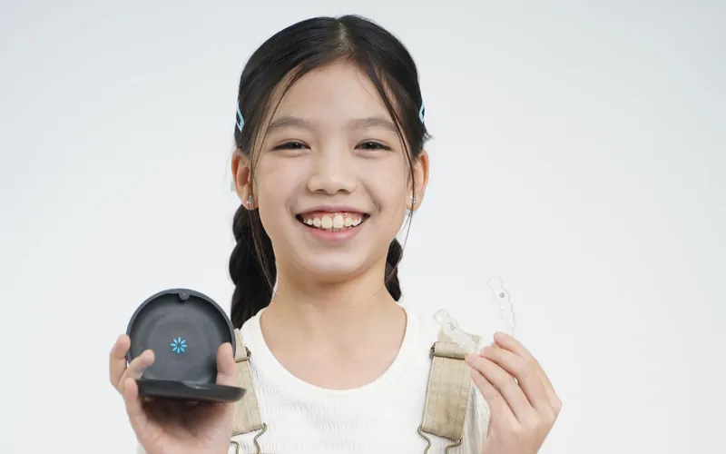A young girl smiling while holding her clear aligner and its case